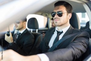 Homme en costume et lunettes noir assurant la sécurité d'une personnalité en voiture