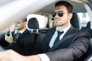 Homme en costume et lunettes noir assurant la sécurité d'une personnalité en voiture